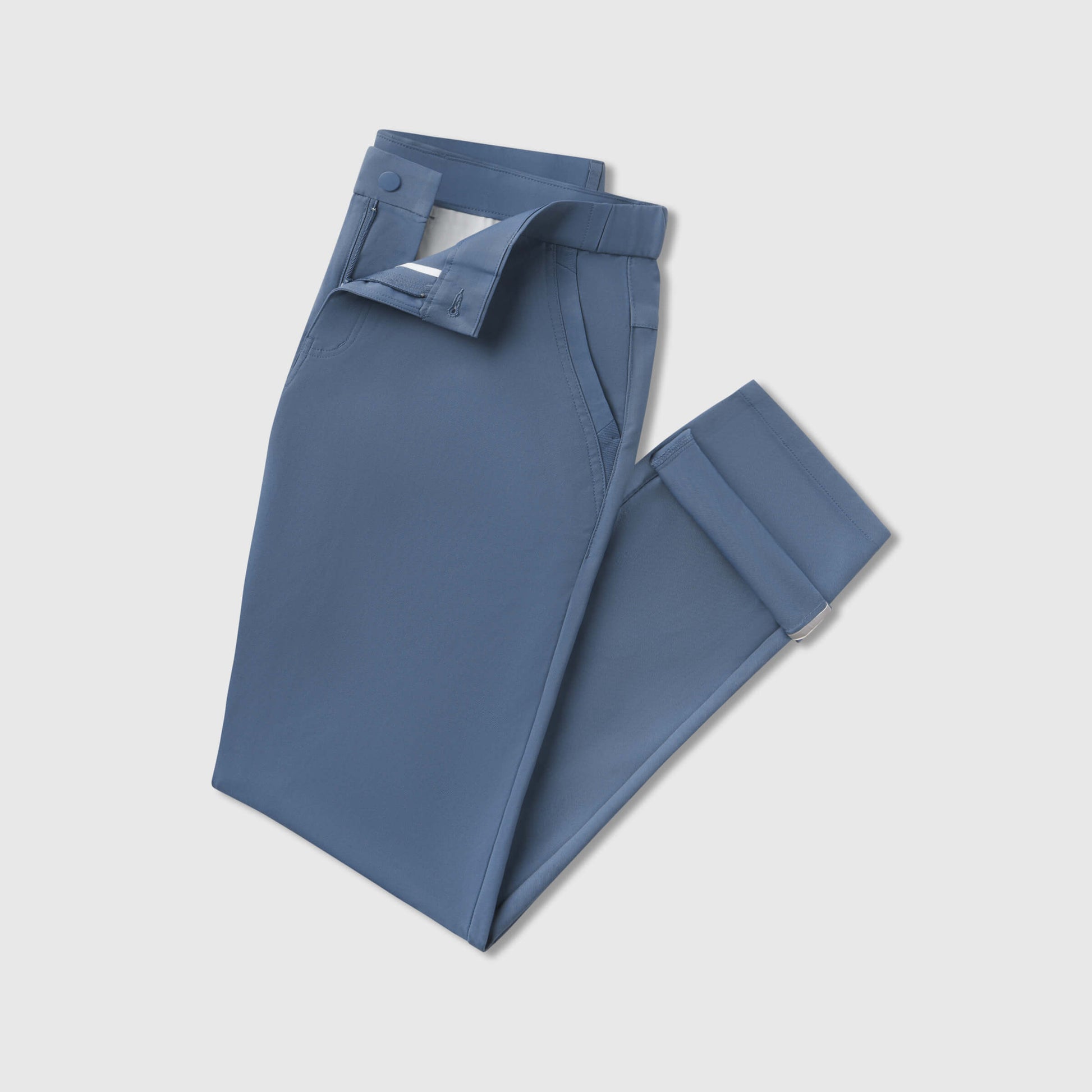 A pair of Jetsetter Tech Pant Slim Fit in blue, neatly folded with the button and zipper partially undone, displayed on a plain light gray background.