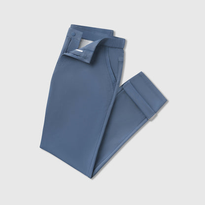 A pair of Jetsetter Tech Pant Slim Fit in blue, neatly folded with the button and zipper partially undone, displayed on a plain light gray background.