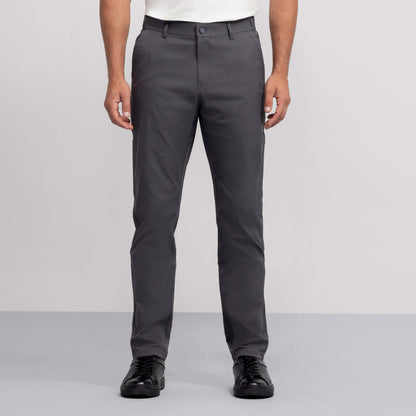 A person wearing Jetsetter Tech Pant Slim Fit in gray, paired with a white shirt and black sneakers, stands against a plain light gray background. The image displays the individual from shoulders to feet.