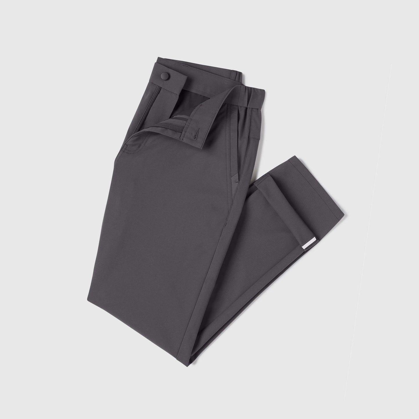 A pair of Jetsetter Tech Pant Slim Fit in dark gray, wrinkle-free with matching fabric belt, neatly folded and displayed on a light gray background.