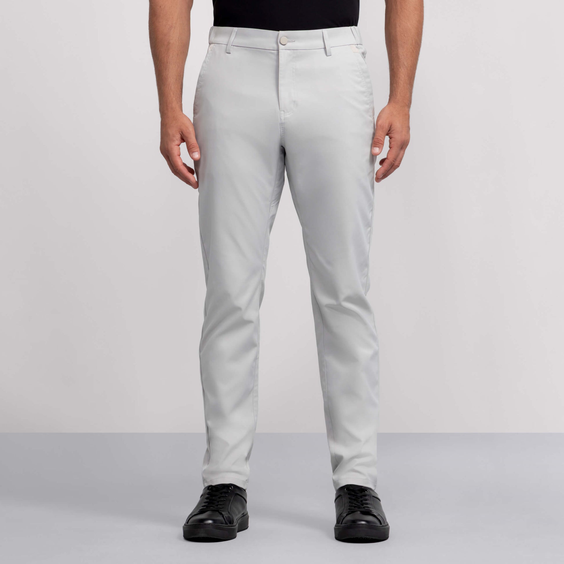 A person wears light gray Jack Archer Jetsetter Tech Pant, a black shirt, and black shoes, standing facing forward against a plain gray background.