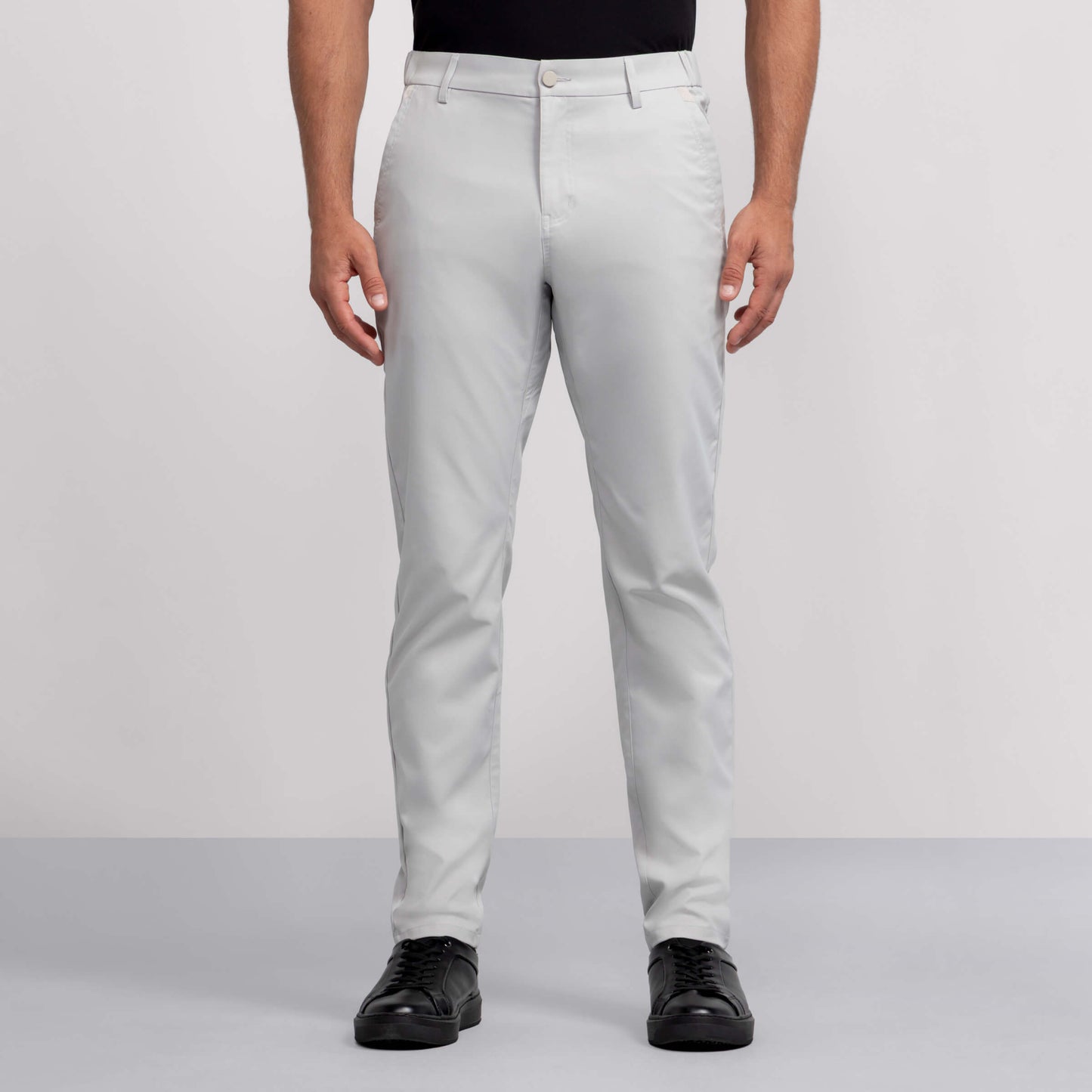 A person wears light gray Jack Archer Jetsetter Tech Pant, a black shirt, and black shoes, standing facing forward against a plain gray background.
