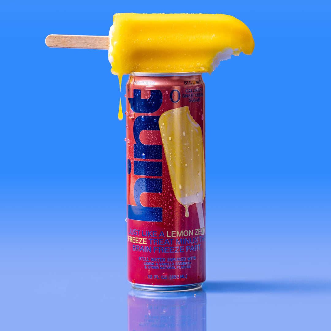 12 oz lemon zest flavored Hint Water can with a melting lemon popsicle balanced on top against a blue background